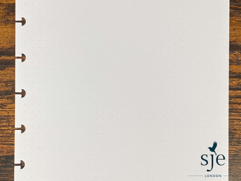 Puede incluir: Un cuaderno blanco con puntos, con una encuadernaci&oacute;n negra y un logotipo de p&aacute;jaro negro que dice "sje london".