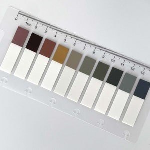 May include: A clear plastic ruler with 14 colour-coded sticky notes. The notes are arranged in a row, with each note having a different colour. The ruler is marked with centimetres and inches.
