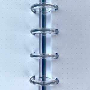May include: Close-up of a white notebook with a dotted grid pattern. The notebook has a clear plastic binding system with four rings.