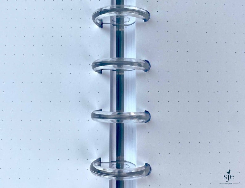 May include: Close-up of a white notebook with a dotted grid pattern. The notebook has a clear plastic binding system with four rings.