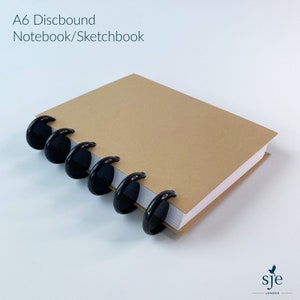 May include: An A6 discbound notebook or sketchbook with a brown cover and black plastic disc binding.