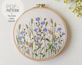 May include: Embroidered hoop art featuring a field of blue and white wildflowers. The hoop is made of wood and has a white fabric background. The embroidery is done in a variety of stitches and colors. The image includes the text "PDF PATTERN + YouTube video tutorial".