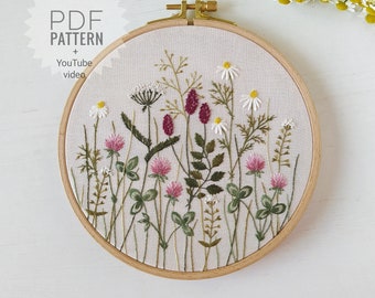 Peut inclure: Broderie florale sur un cercle en bois, représentant diverses fleurs sauvages vertes, roses, blanches et bordeaux. Le texte "PDF PATTERN + YouTube video" est visible en haut à gauche.