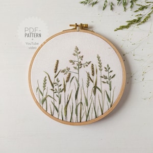 Könnte beinhalten: Ein runder Stickrahmen mit einem botanischen Design aus grünen Gräsern und Weizenähren. Das Kunstwerk ist auf cremefarbenem Stoff gestickt und von einem natürlichen Holzrahmen eingefasst. Der Text auf dem Bild lautet "PDF Pattern + YouTube video."