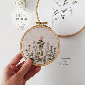 Può includere: Due motivi di ricamo su telaio con disegni floreali. Il telaio più piccolo mostra un gruppo di fiori rosa e foglie verdi. Il telaio più grande mostra un disegno a forma di cuore con fiori rosa e foglie verdi. Il testo "PDF-PATTERN + YouTube video tutorial" è visibile nell'immagine.