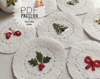 May include: A collection of circular white fabric pieces featuring various hand-embroidered Christmas motifs including a tree, holly, mittens, a bow, and a gift. The text PDF PATTERN + YouTube video is overlaid on the image. Several white buttons are visible.