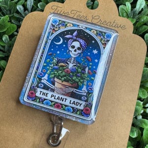 May include: A blue and white glitter badge holder with a skeleton holding a pot of flowers. The badge holder has the text "The Plant Lady" on it.