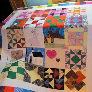 May include: A patchwork quilt featuring a variety of colourful squares and patterns. The quilt has a central panel with a house, a church, a heart, and a dancing couple. The quilt is made from a range of fabrics, including floral prints, geometric patterns, and plain colours.