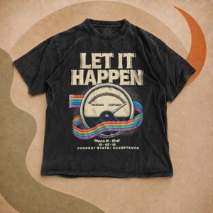 Può includere: Una t-shirt a maniche corte color nero carbone con la scritta LET IT HAPPEN sopra il grafico di un misuratore con le etichette RESISTANCE e ACCEPTANCE. Un nastro color arcobaleno avvolge il misuratore, con la scritta TRACK 01-07:47 10-03-15 CURRENT STATE: ACCEPTANCE sotto.