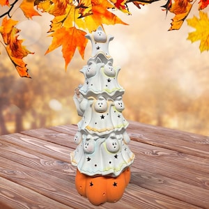 May include: A white ceramic Halloween tree with a pumpkin base. The tree is decorated with ghosts and stars.