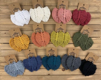May include: Assortment of handmade macrame earrings in various colors, including white, pink, red, yellow, orange, green, blue, gray, and black. The earrings are all in the shape of a leaf and have a fringe detail.