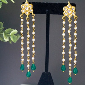 May include: Gold earrings with a floral design and white pearl chains, ending with green teardrop-shaped stones.