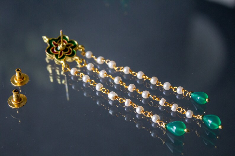 May include: Gold earrings with a green and red floral design, white pearl beads, and green gemstone drops.