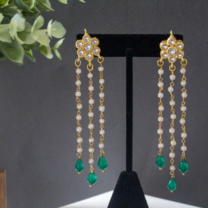 May include: Gold earrings with a floral design and three strands of pearl beads, each ending with a green teardrop-shaped stone.