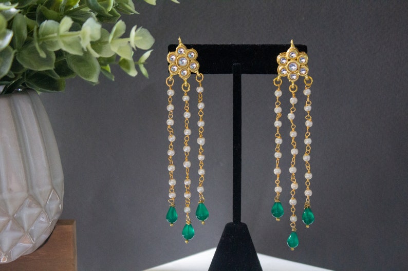 May include: Gold earrings with a floral design and three strands of pearl beads, each ending with a green teardrop-shaped stone.