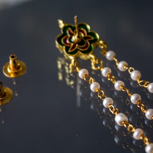 May include: A pair of gold earring backs and a gold earring with a green, red and white enamel flower design and a chain of white pearls.