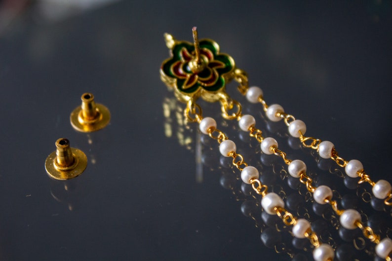 May include: A pair of gold earring backs and a gold earring with a green, red and white enamel flower design and a chain of white pearls.