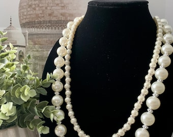 May include: A double strand pearl necklace with large and small pearls. The necklace is white and is displayed on a black velvet stand.