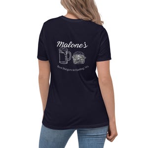 Puede incluir: Camiseta azul marino con un gráfico blanco de una jarra de cerveza y una hamburguesa. El texto "Malone's Best Burgers in Hastings, MA" también está impreso. La camiseta es de un material suave.