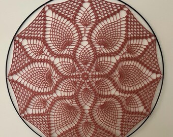 May include: A pink crocheted doily with a delicate floral pattern is displayed on a black metal hoop.