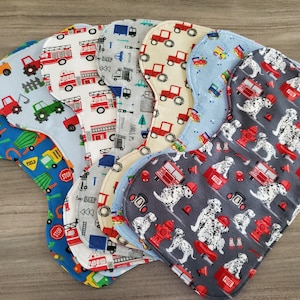 May include: A set of ten colorful baby bibs with different patterns. The bibs feature various designs, including fire trucks, dalmatian dogs, and construction vehicles. The bibs are made of soft, absorbent fabric and are perfect for keeping baby's clothes clean during mealtime.