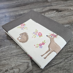 May include: A white ceramic mug with a black handle and the text "But First, Coffee" in a bold, black font. The mug is set against a blurred background, suggesting a cozy setting.