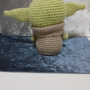 May include: A crocheted green and brown plush toy resembling a character from the Star Wars franchise. The toy has large ears and a small body.