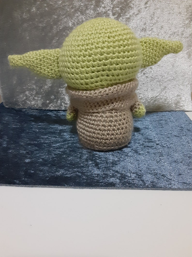 May include: A crocheted green and brown plush toy resembling a character from the Star Wars franchise. The toy has large ears and a small body.