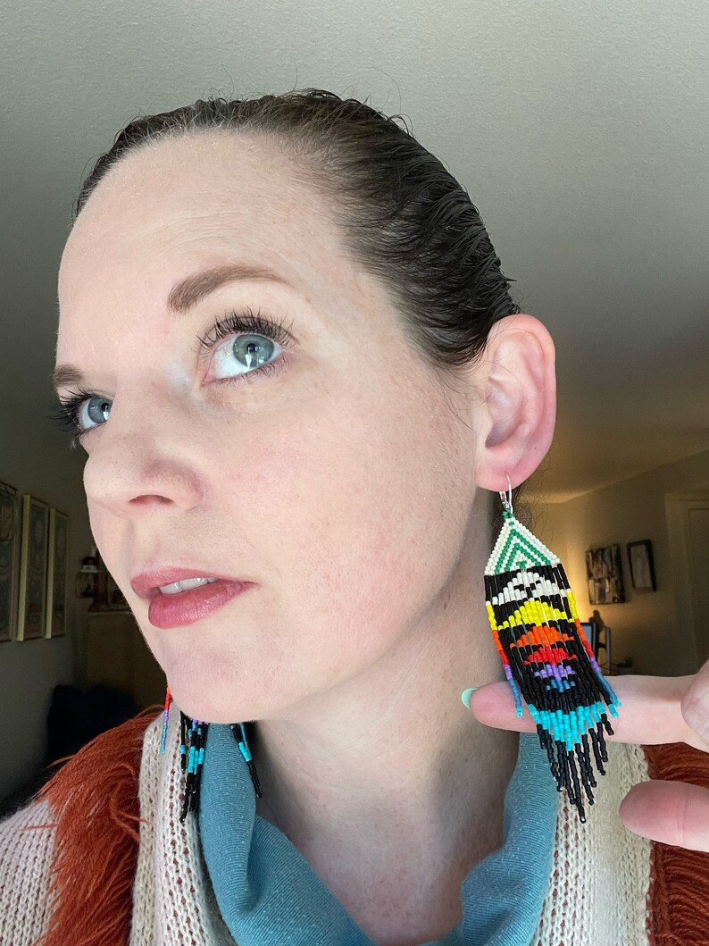 May include: A pair of long, colorful beaded earrings with a geometric pattern. The earrings are black, white, green, blue, yellow, orange, and red.