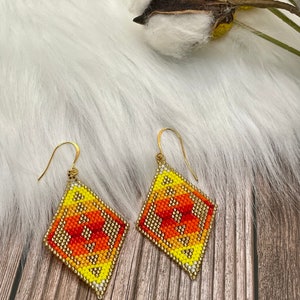 May include: A pair of yellow, orange, and white beaded earrings with gold hooks. The earrings are in the shape of a diamond.