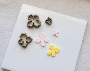 Peut inclure: Un ensemble de six emporte-pièces en forme de fleur sur une surface blanche. Les emporte-pièces sont en métal et de différentes tailles. Le plus grand emporte-pièce est brun, les deux suivants sont roses et les trois plus petits sont jaunes.