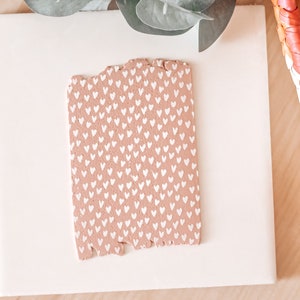 May include: A pink and white patterned tile with a heart design. The tile is on a white surface with a paintbrush.