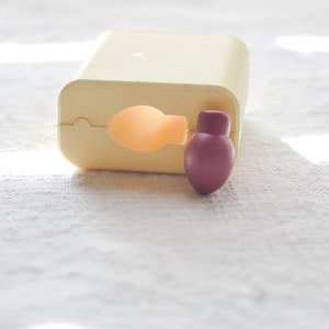 May include: A light beige plastic dispenser with a round, burgundy-colored cap. The dispenser is open and the cap is partially removed.
