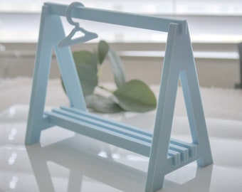 May include: A light blue wooden display stand with a hanger for jewellery or small clothing items. The stand has three shelves and a triangular base.