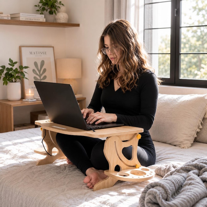 May include: A light-colored wooden laptop desk with a curved top surface and adjustable side supports. The desk features integrated circular cutouts on the side panels for storage and yellow adjustment knobs, designed for use on a flat surface.