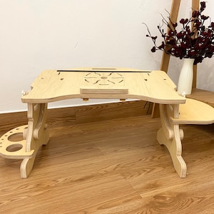 May include: A light-colored wooden laptop desk with an adjustable surface, featuring a central circular cutout design, a small front ledge, and two side attachments, one with circular holes and one with a smooth, rounded surface extension.
