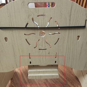 May include: A wooden baby playpen with a light brown finish. The playpen has a black metal bar across the top and a wooden shelf on the bottom. The shelf has two small cutouts on either side.