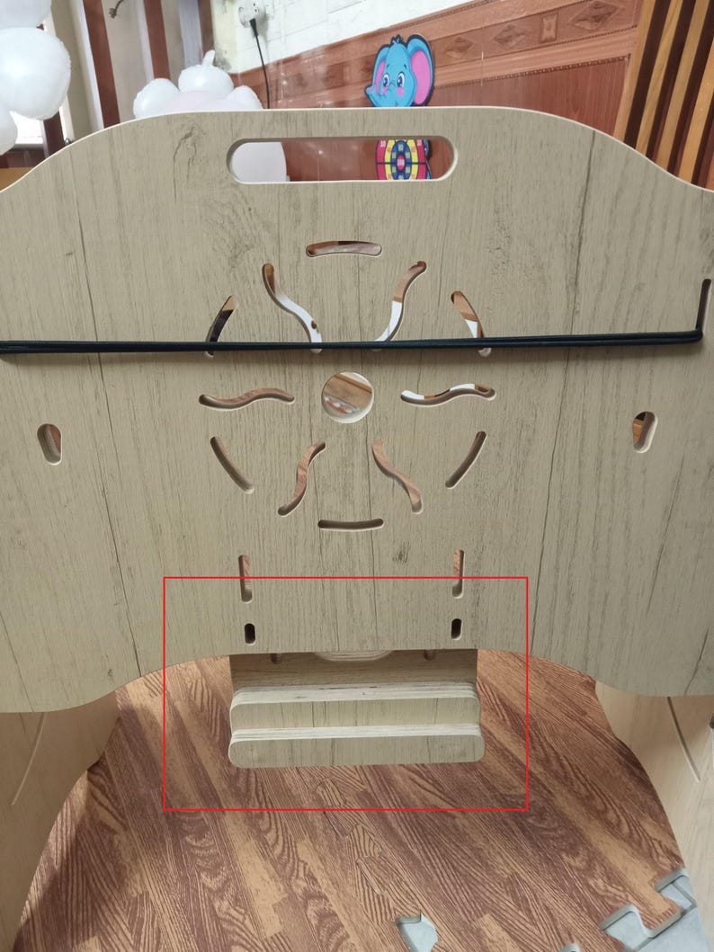 May include: A wooden baby playpen with a light brown finish. The playpen has a black metal bar across the top and a wooden shelf on the bottom. The shelf has two small cutouts on either side.