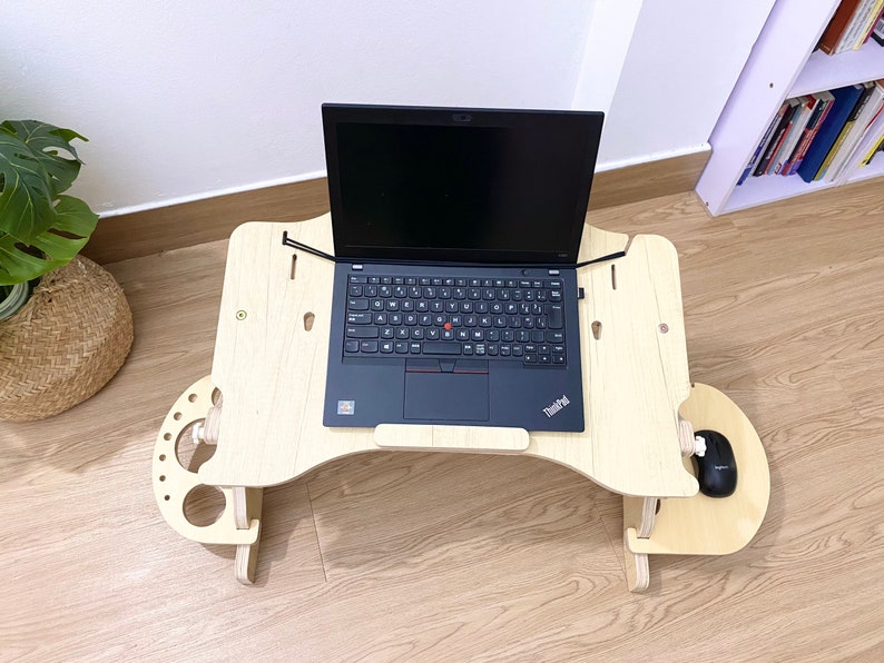 May include: A wooden laptop stand with a black laptop on top. The stand has a built-in mouse pad and a cup holder. The laptop has a black keyboard and a black touchpad.