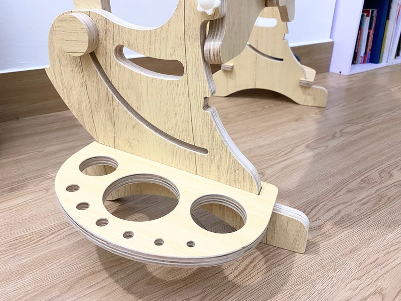 May include: A wooden stand with a curved top and a base with multiple circular cutouts. The stand is made of light wood with a wood grain pattern.