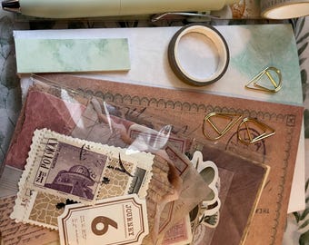 May include: A stationery set featuring a light green pen, washi tape, paper clips, and various decorative paper elements. The set includes stamps, stickers, and paper with vintage-style designs and the word "JOURNEY".