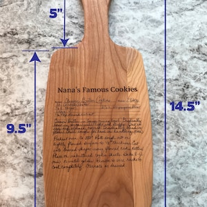 Op de afbeelding: Een houten snijplank met een gegraveerd recept voor Nana's beroemde koekjes. De plank is 36,8 cm lang, 24,1 cm breed en 15,2 cm hoog. Het recept bevat ingredi&euml;nten zoals boter, suiker, eieren en amandel extract.