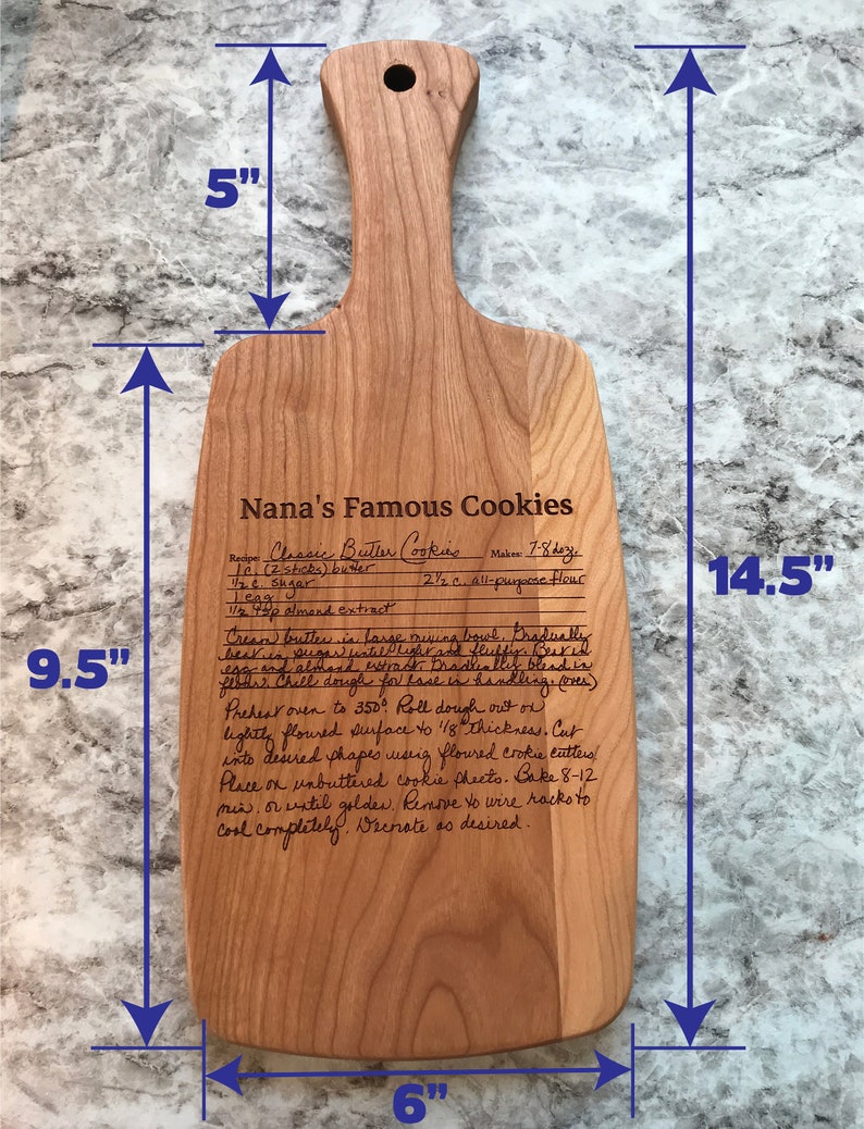 Op de afbeelding: Een houten snijplank met een gegraveerd recept voor Nana's beroemde koekjes. De plank is 36,8 cm lang, 24,1 cm breed en 15,2 cm hoog. Het recept bevat ingredi&euml;nten zoals boter, suiker, eieren en amandel extract.