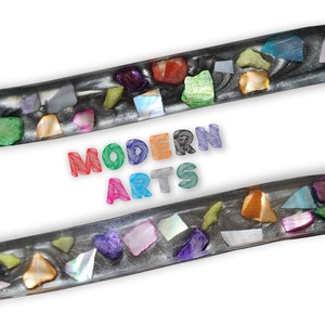 May include: Two silver resin bookmarks with a wavy design. The bookmarks are embedded with colorful, iridescent, and pearlescent pieces of glass and shell. The text "MODERN ARTS" is written in colorful letters below the bookmarks.