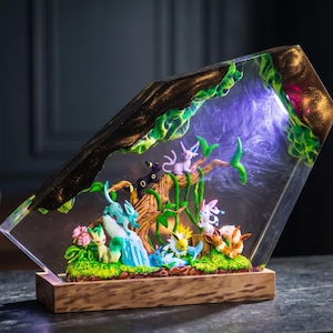 May include: A trapezoidal resin display featuring multiple small colourful creature figurines nestled within a wooden base. The clear resin contains swirling purple light effects, green foliage, and a central tree structure, creating a diorama scene.