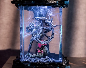 Op de afbeelding: Een rechthoekige, verlichte displaycase met een Predator en een Alien in een gevechtsscène. De figuren zijn gedetailleerd en donker, tegen een blauwe, rokerige achtergrond. De case heeft een zwarte, getextureerde basis en bovenkant.