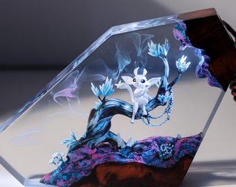 Puede incluir: Escultura de resina transparente con una criatura blanca sobre una rama de árbol, con detalles azules y morados. La escultura tiene una base de madera y un cable negro. La obra de arte está iluminada con un brillo suave.