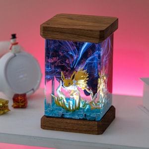 May include: A rectangular lamp with a wooden top and base. The lamp's body is a clear resin with a yellow and white cartoon character inside, surrounded by blue and purple swirling patterns. The lamp sits on a white shelf.