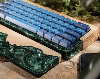 May include: A custom mechanical keyboard with blue keycaps and a wooden frame. The keyboard rests on a green and black resin base. A black mouse and mousepad are also visible.