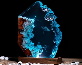 Könnte beinhalten: Eine blaue Harzskulptur einer Manta-Rochen, die im Ozean schwimmt. Die Skulptur steht auf einem Holzsockel mit dem Text "BREAKWOODEN" auf der Vorderseite.